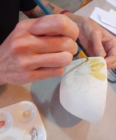 Detalle del proceso creativo: manos pintando una flor en cerámica durante un retiro artístico en Asturias